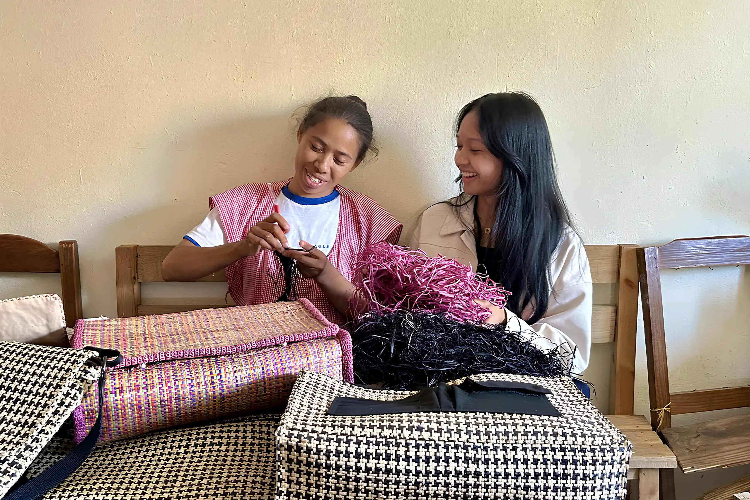 Synoet Founder - Miah Rabemananjara Two women sit on a bench, chatting and smiling, with bags beside them.